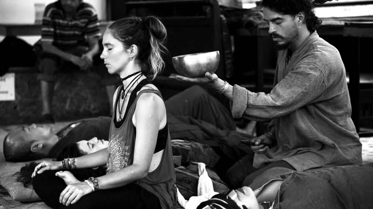 a sound and touch session, singing bowl held above a seated participant, others reclining nearby